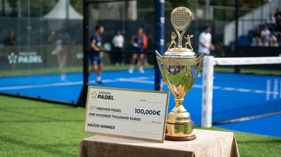 Trofeo y cheque de premio de un torneo Major de Premier Pádel junto a una pista profesional
